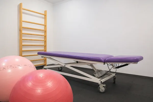 Sala rehabilitacji: drabinka gimnastyczna, kozetka z regulacją wysokości i dwie piłki gimnastyczne na macie.